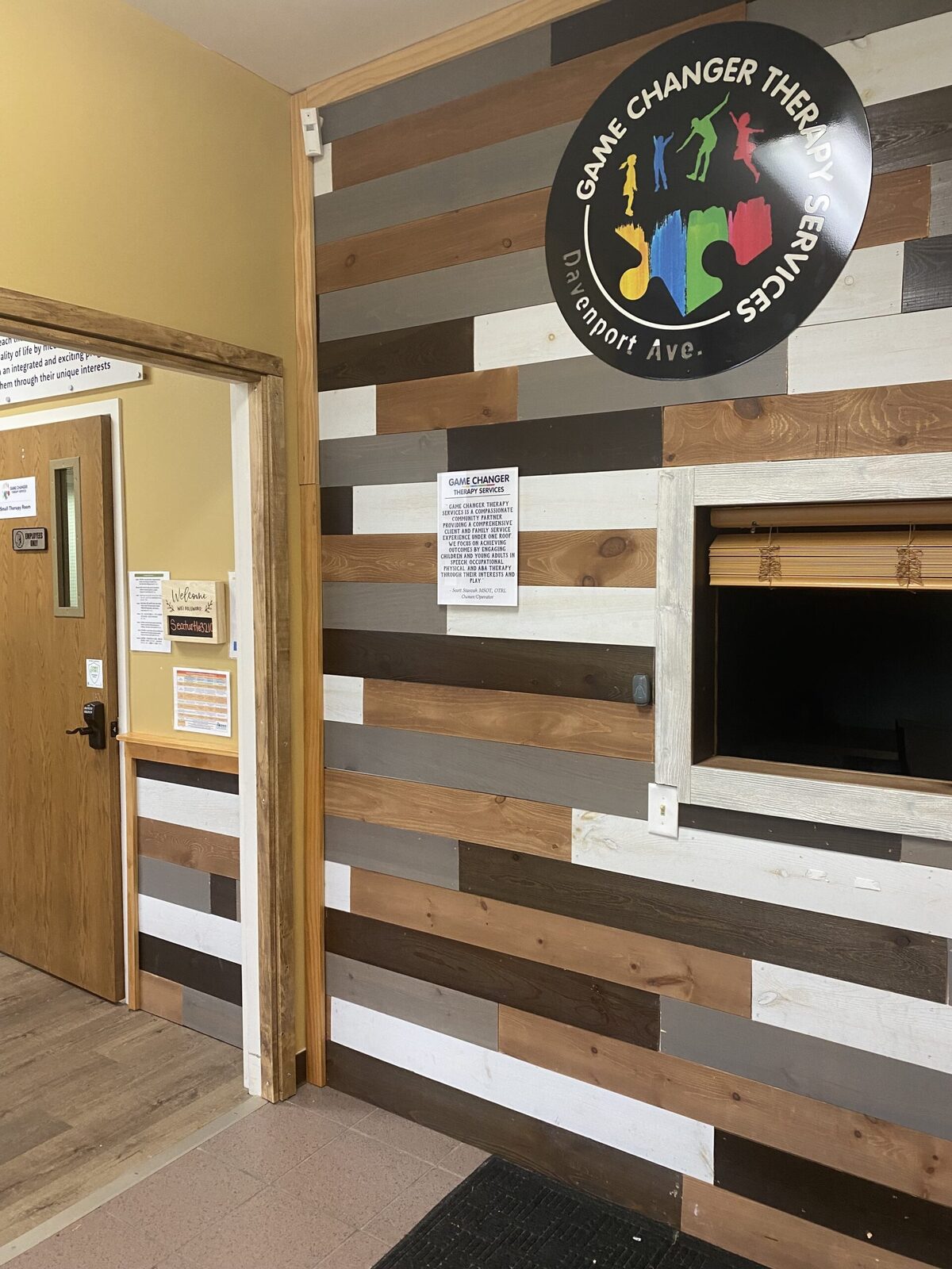 A reclaimed-plank welcome wall with the Davenport Avenue Game Changer Therapy Services sign above a check-in window