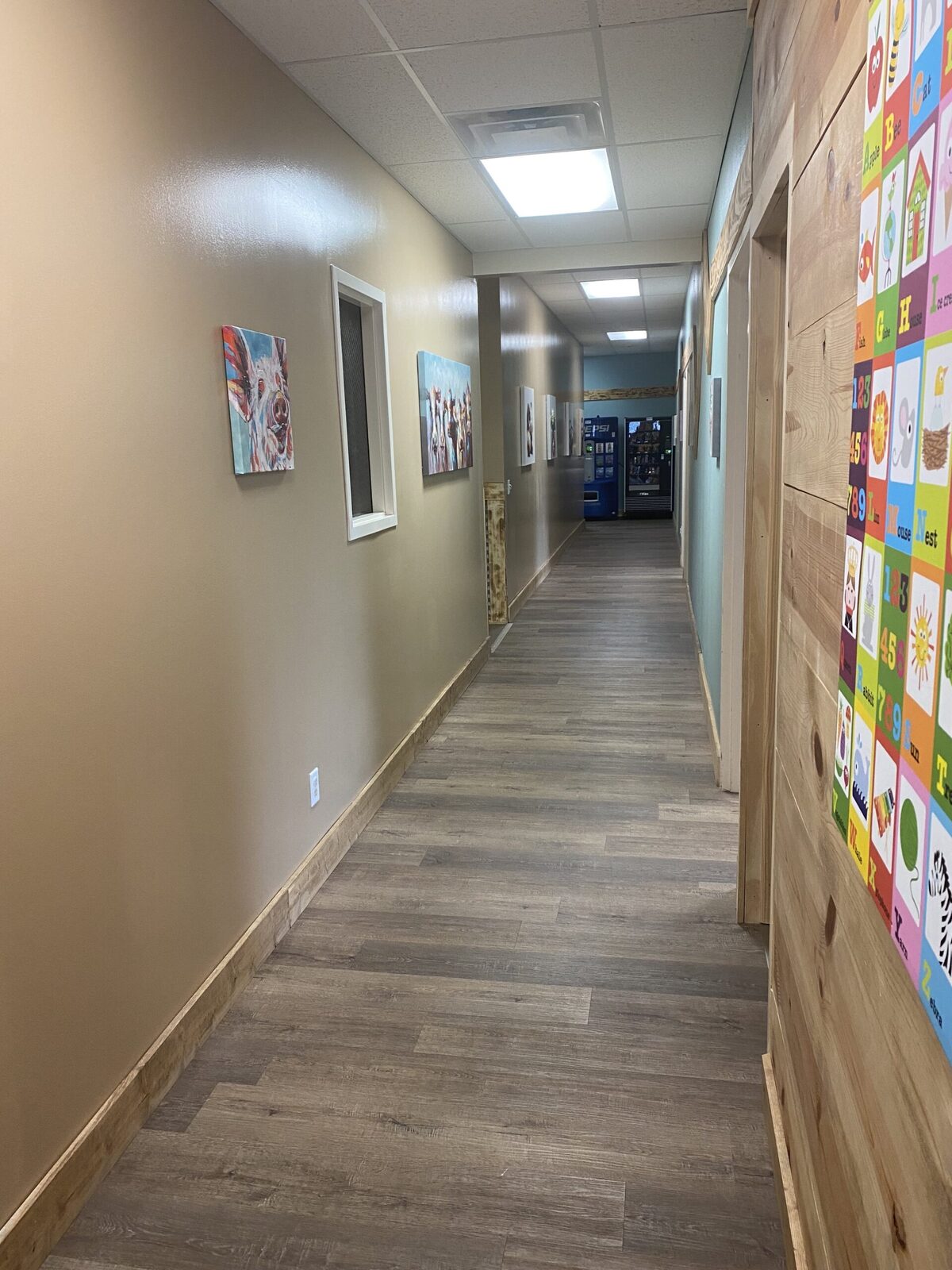 A clinic corridor hung with bright animal canvases, with an oversized alphabet and numbers panel mounted on a plank wall