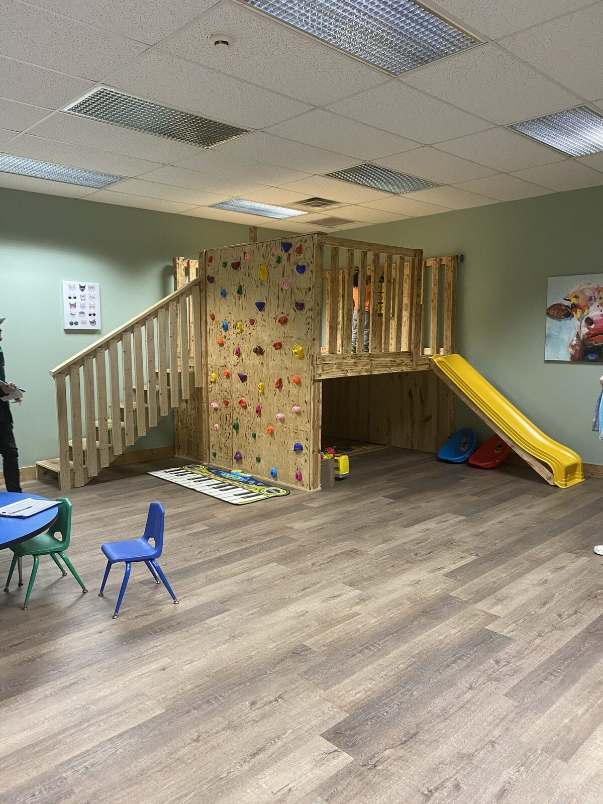 An indoor climbing wall, wooden play loft and yellow slide inside a Game Changer clinic gym