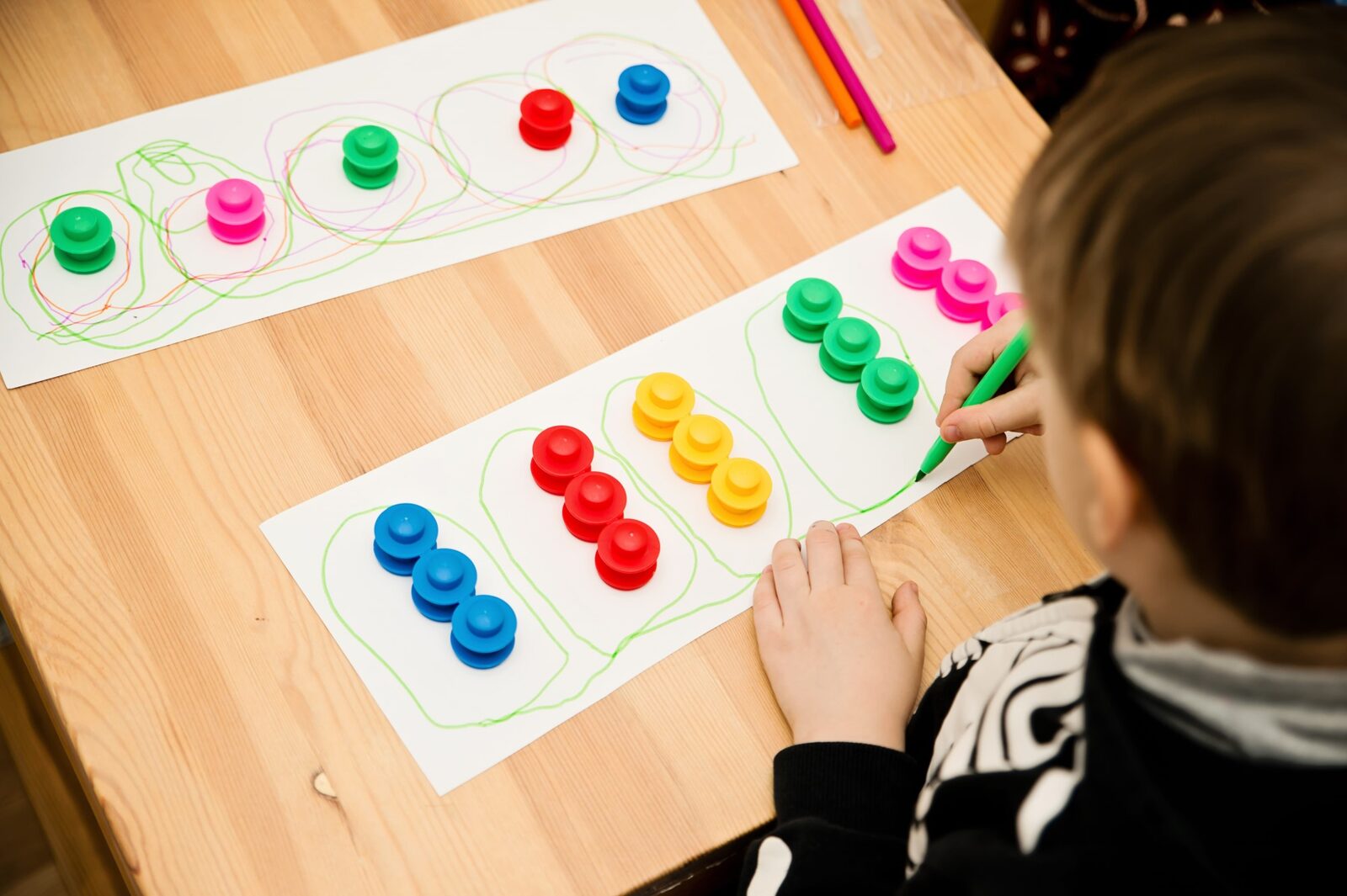 A child drawing green circles around rows of coloured stacking blocks during a table-top therapy activity