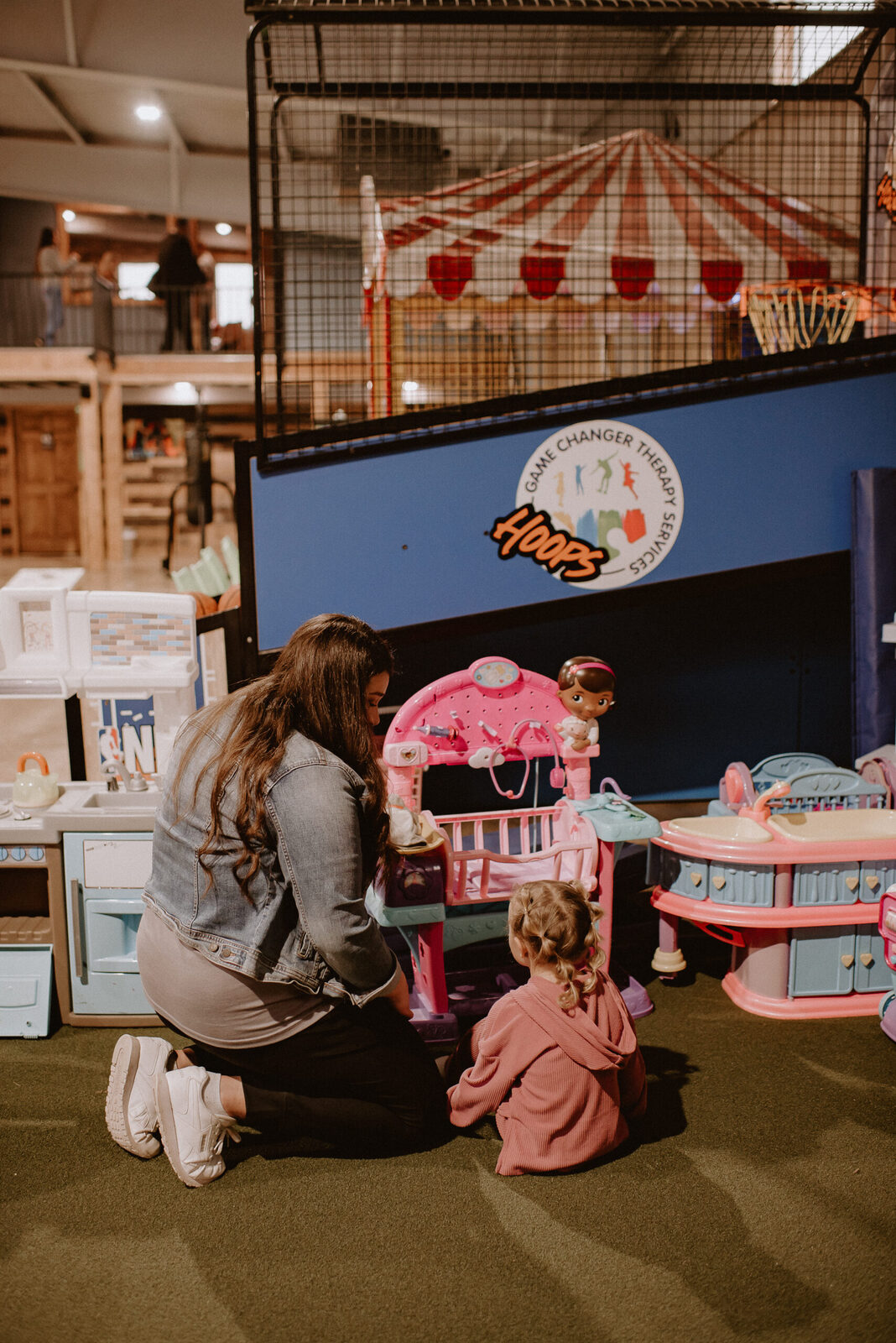 A therapist kneeling beside a child in a colorful play-based therapy room