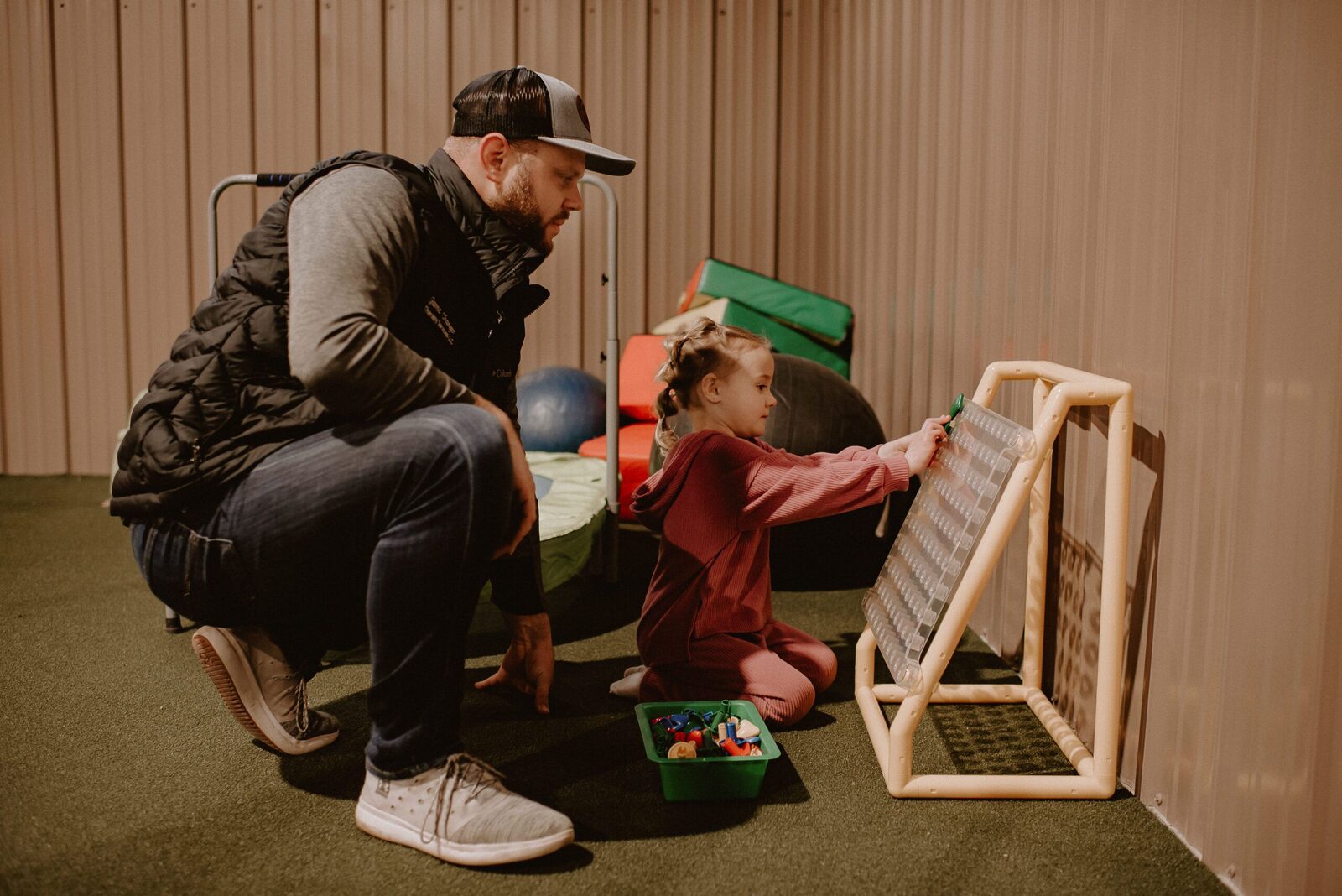 Therapist and child working together at a wooden activity frame with exercise balls