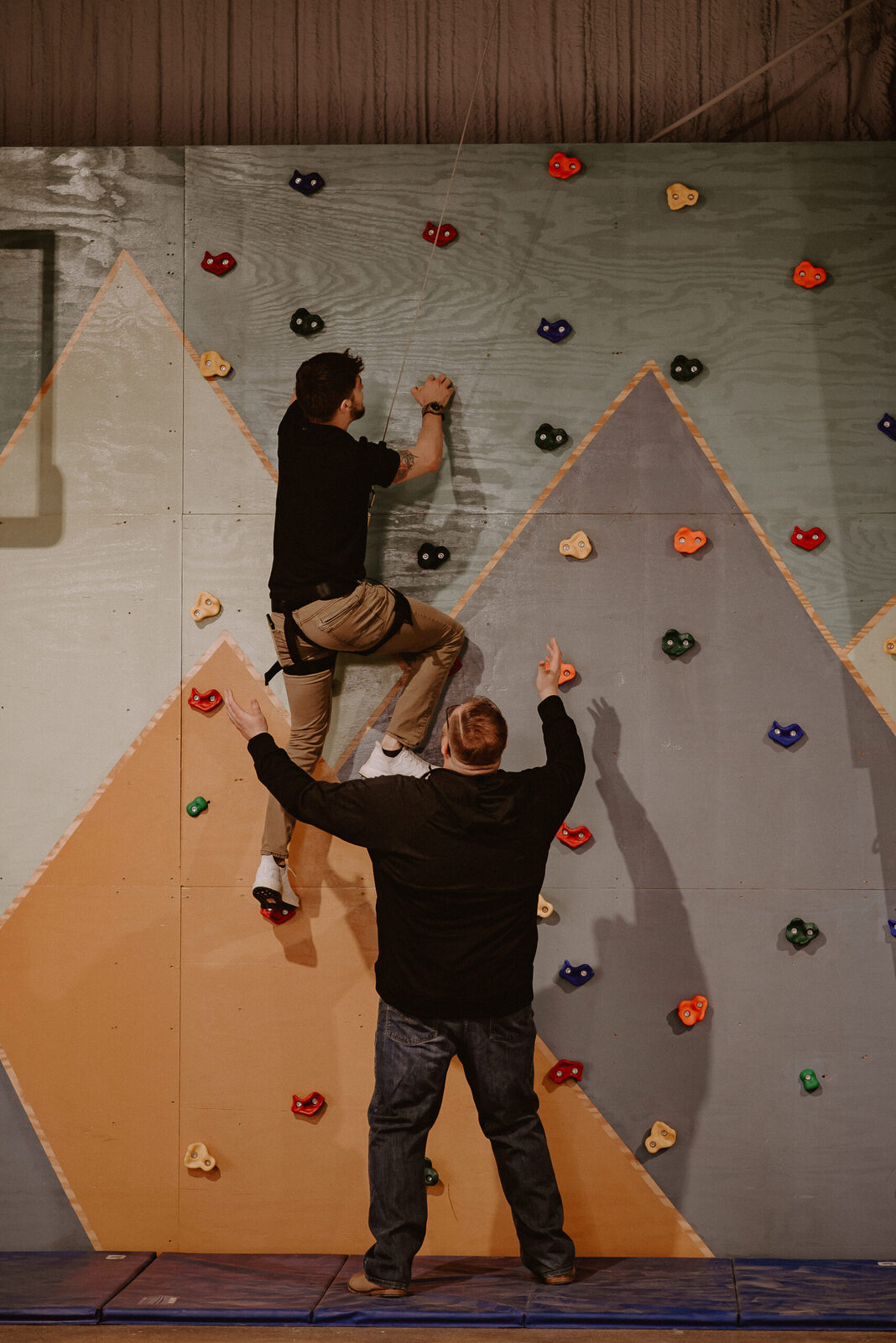 An adult and child working together on a large triangular climbing wall