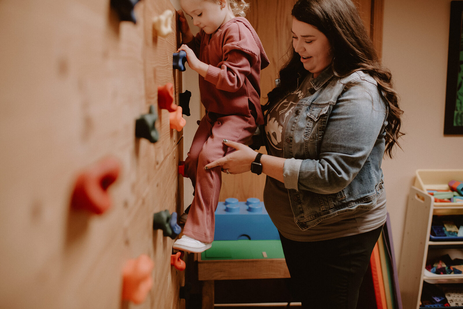 A child climbing a peg wall while a therapist spots from behind